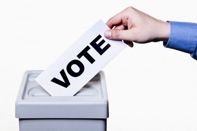 A man putting a ballot with the word VOTE written on it into a ballot box, close-up hands --- Image by © Epoxydude/fstop/Corbis